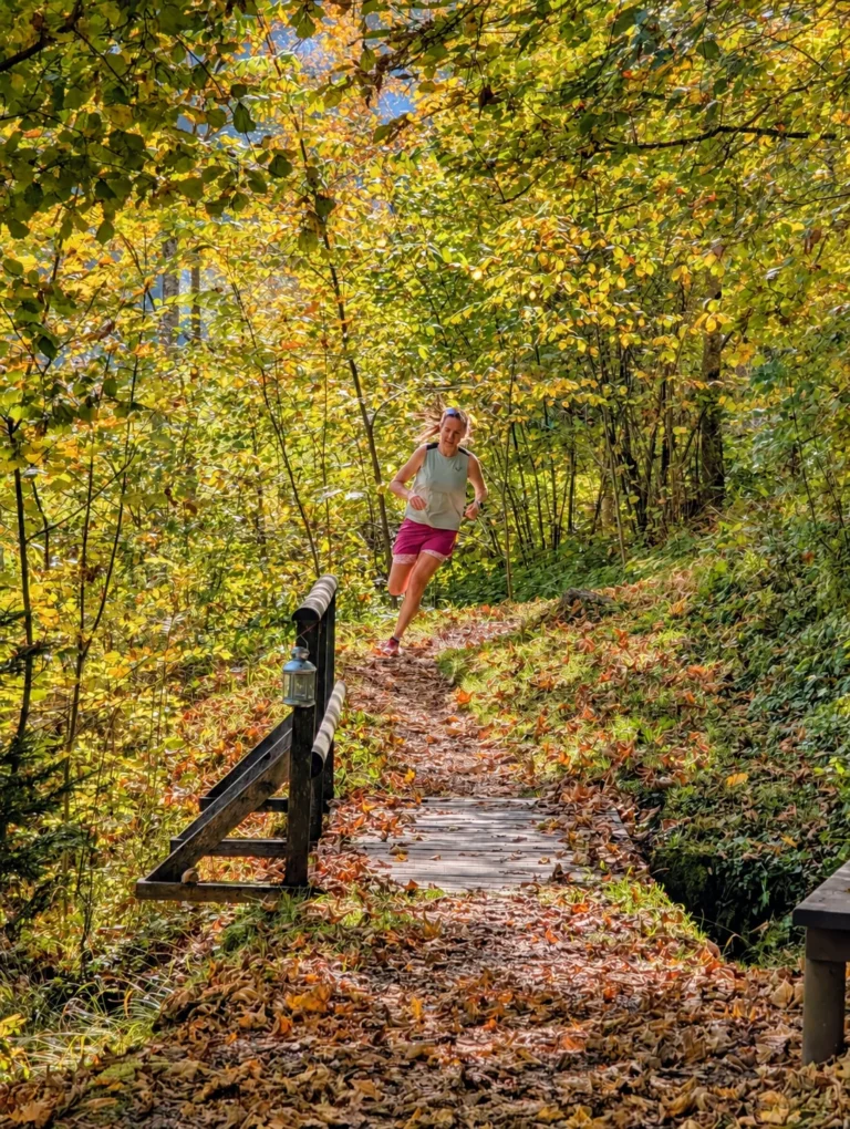 Trailrunning – bergab mit mehr Vertrauen | Sonntag Trailrunnerin läuft auf einem herbstlichen Waldpfad über eine kleine Holzbrücke bergab