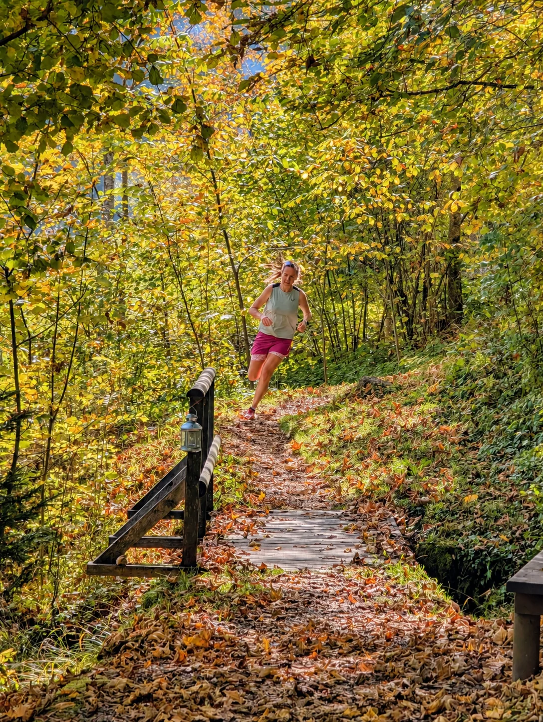 Trailrunnerin läuft auf einem herbstlichen Waldpfad über eine kleine Holzbrücke bergab