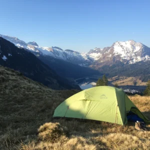 Grünes Biwakzelt auf einer Bergwiese mit Blick auf die umliegenden Gipfel